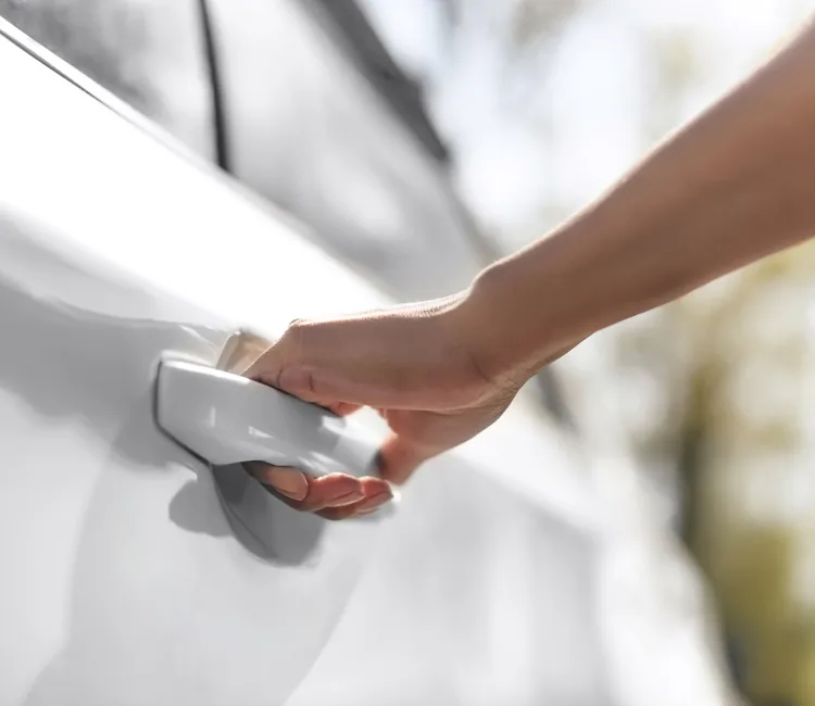 Hand holding a white door handle with sunlight casting shadows on white surface.
