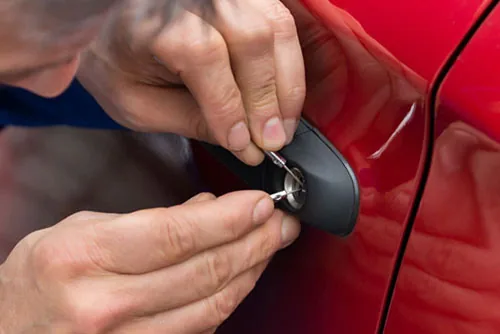 Locksmith technician working on a red car door lock with tools.